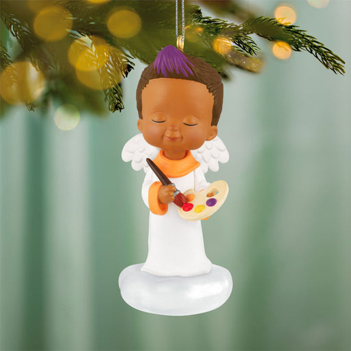 Decorative angel ornament with a child holding a paintbrush and palette, hanging on a Christmas tree.