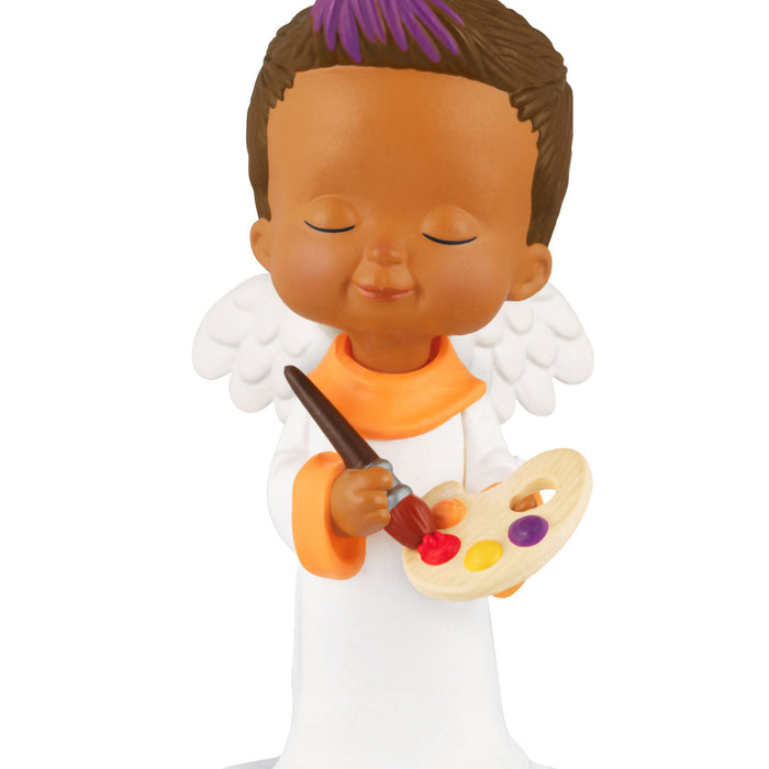 Figurine of a child with angel wings holding a paintbrush and palette on a white background