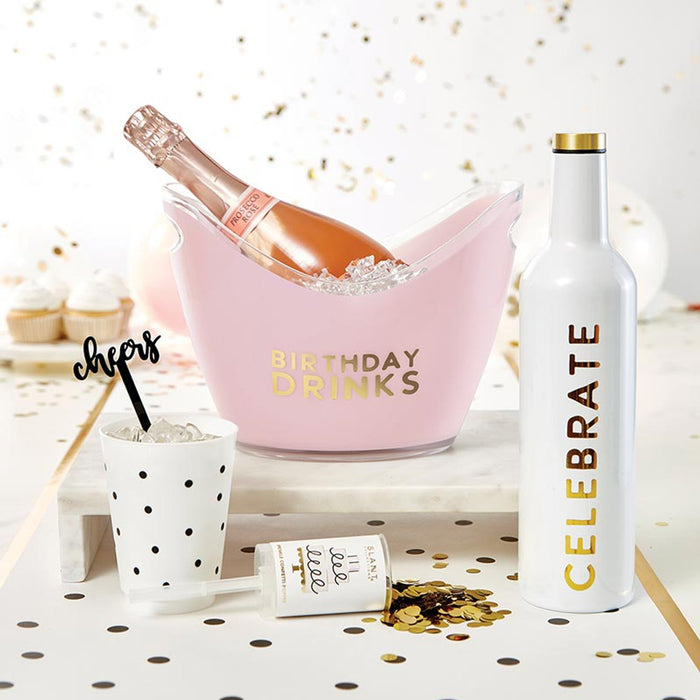 Bottle of champagne in a pink bucket labeled 'Birthday Drinks' with a 'Celebrate' bottle and confetti on a decorative surface.
