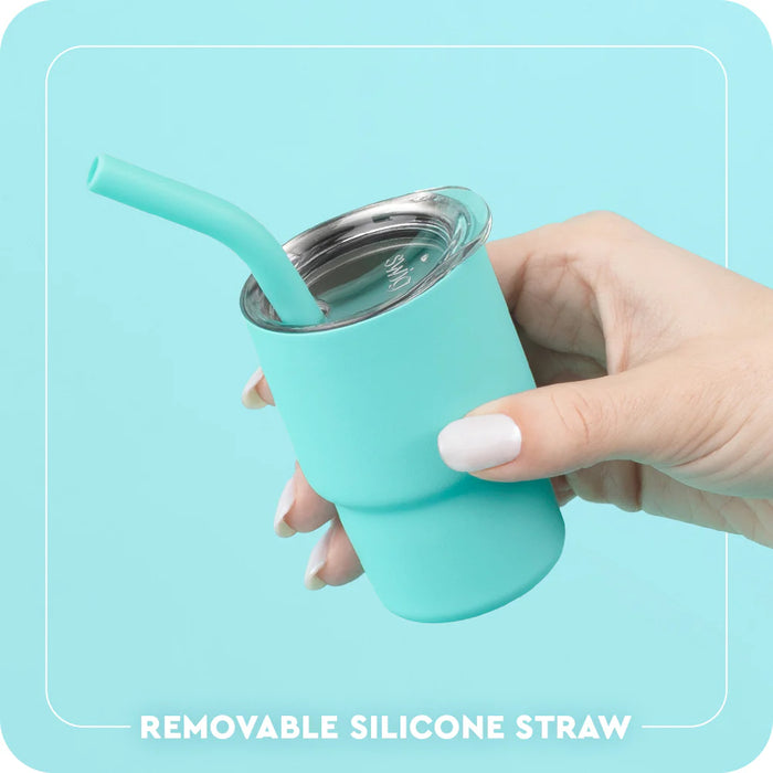 Turquoise tumbler with a removable silicone straw held by a hand against a light blue background.