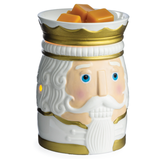 A ceramic nutcracker-shaped wax warmer with a white face, gold trim, and blue eyes, topped with three orange wax melts on a white background.