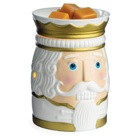 A ceramic nutcracker-shaped wax warmer with a white face, gold trim, and blue eyes, topped with three orange wax melts on a white background.
