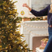Person decorating a Christmas tree with an ornament in a festive living room.