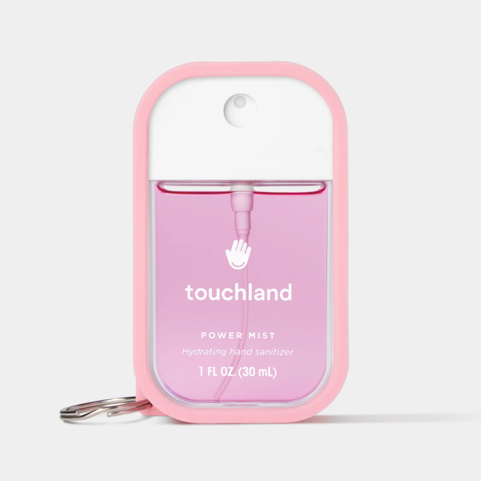 A pink silicone protective case for a Touchland Power Mist hand sanitizer, featuring a white cap, clear bottle showing pink liquid, and a silver keychain ring, on a light gray background.