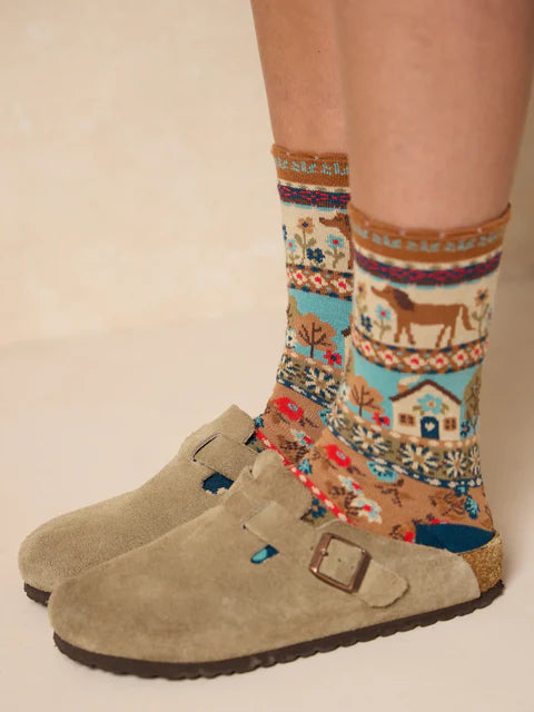 Beige suede shoes with a person wearing patterned socks on a beige background