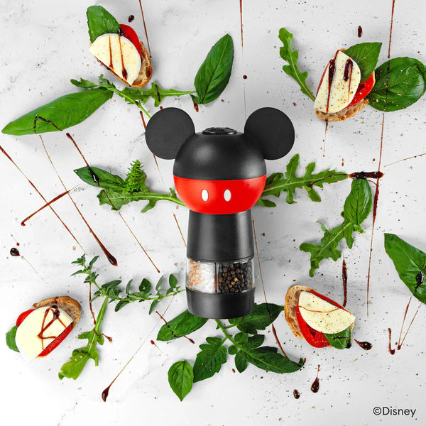 Pepper grinder with Mickey Mouse design surrounded by food and greens on a light surface