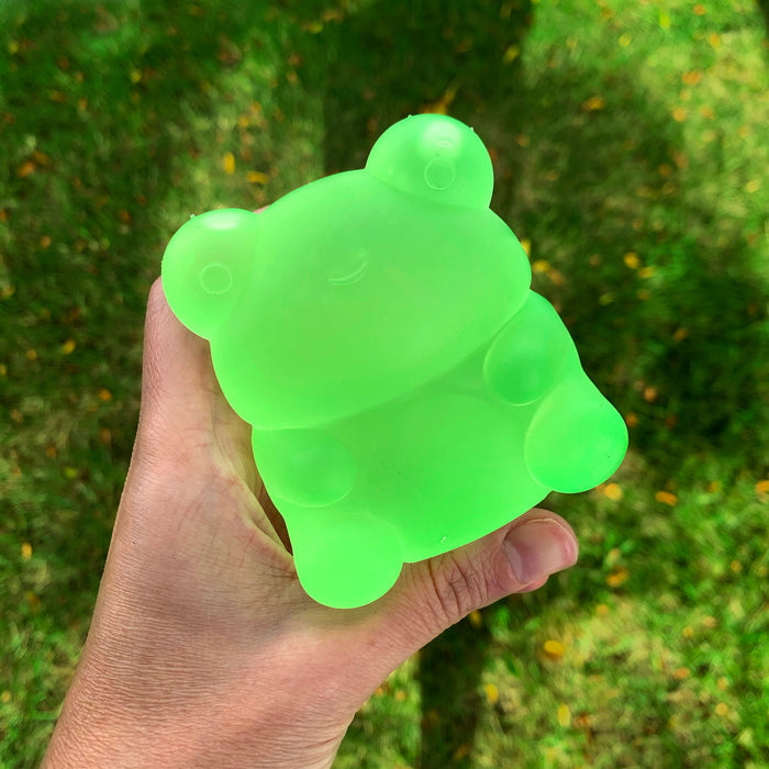 Hand holding a green bear-shaped ice cube tray against a grassy background
