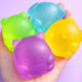 Four colorful silicone sanding blocks shaped like animals held in a hand against a light purple background.