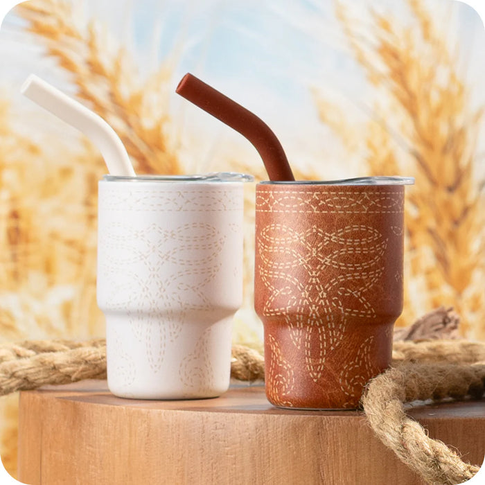 Two ceramic cups with straws on a wooden surface with a blurred natural background
