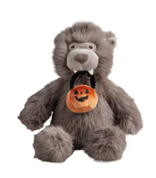 A gray plush stuffed animal with a furry body, small white fangs, and a black neck ribbon holding an orange pumpkin-shaped Halloween bucket bag, shown on a plain white background.