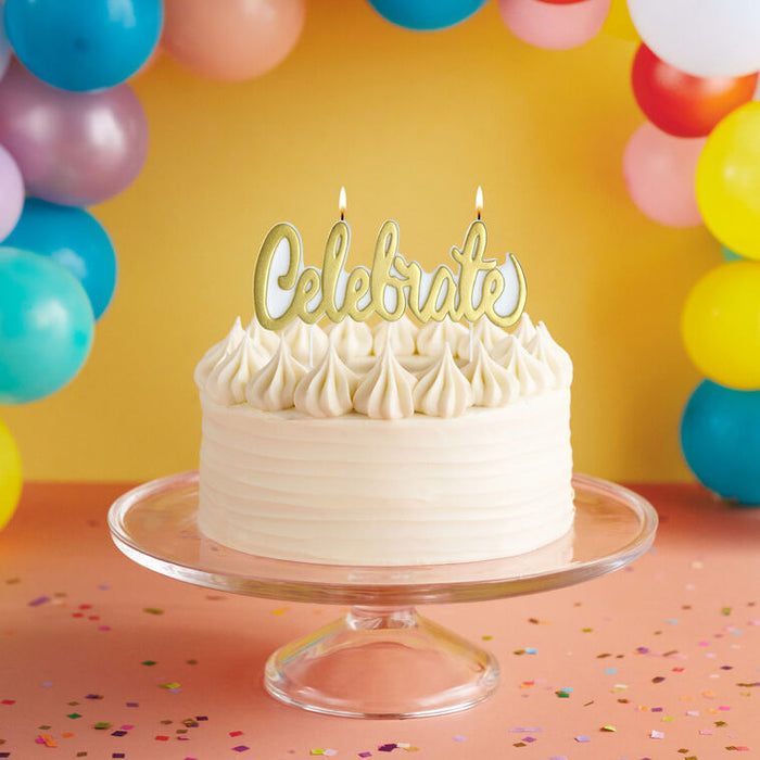 White cake with 'Celebrate' candle on a clear stand against a colorful balloon background