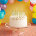 White cake with 'Celebrate' candle on a clear stand against a colorful balloon background