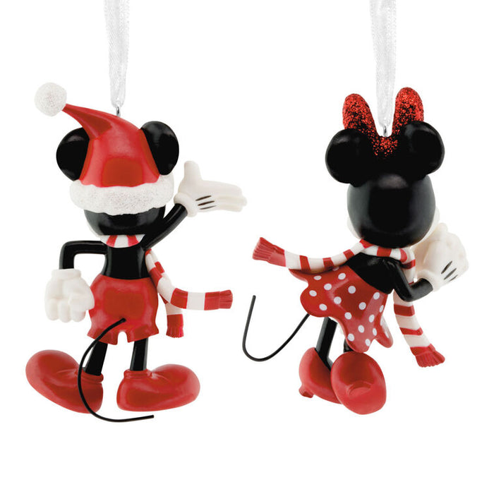 A pair of Mickey and Minnie Mouse Christmas ornaments shown from opposite sides on a plain white background. One ornament depicts Mickey wearing a red Santa hat and red outfit with a red-and-white striped scarf, and the other depicts Minnie wearing a red polka-dot dress, red-and-white striped scarf, and red glittery bow.