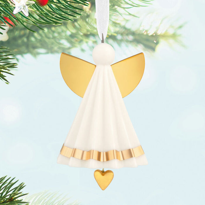 Angel ornament with gold wings and a heart detail, hanging from a Christmas tree.