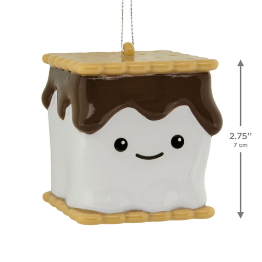 A s'mores-themed ceramic ornament shaped like a marshmallow with chocolate drizzle and a graham cracker border, shown with a hanging string and a vertical dimension marker indicating 2.75 inches (7 cm) height on a white background.