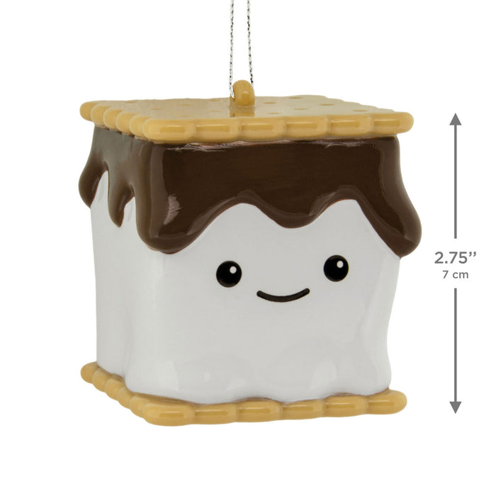 A s'mores-themed ceramic ornament shaped like a marshmallow with chocolate drizzle and a graham cracker border, shown with a hanging string and a vertical dimension marker indicating 2.75 inches (7 cm) height on a white background.