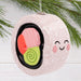 Decorative ornament shaped like a smiling rice ball with pink salmon and green wasabi on a white background.