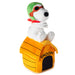 A plush toy of Snoopy sitting on top of his yellow dog house, wearing a green helmet and red goggles, photographed against a solid white background.
