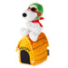 A plush Snoopy figure wearing a green hat and red scarf, sitting on top of a yellow dog house with black stripes and the word 'SNOOPY' on the front, photographed on a white background.