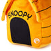 A close-up of an orange plush dog house shaped like Snoopy's house, with 'SNOOPY' embroidered in black on the front, a black arched doorway, and black line details on the side. A small circular Snoopy logo patch is visible near the bottom right.