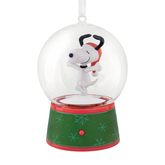 A Snoopy snow globe ornament featuring Snoopy hugging his dog friend inside a clear glass globe, mounted on a green and red holiday-themed base with snowflake patterns.