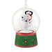 A Snoopy snow globe ornament featuring Snoopy hugging his dog friend inside a clear glass globe, mounted on a green and red holiday-themed base with snowflake patterns.