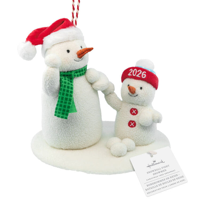 Hallmark 2026 Family Snowman Christmas ornament featuring a large white plush snowman with a red Santa hat and green scarf next to a smaller white plush snowman wearing a red 2026 hat, on a white base with a hanging tag.