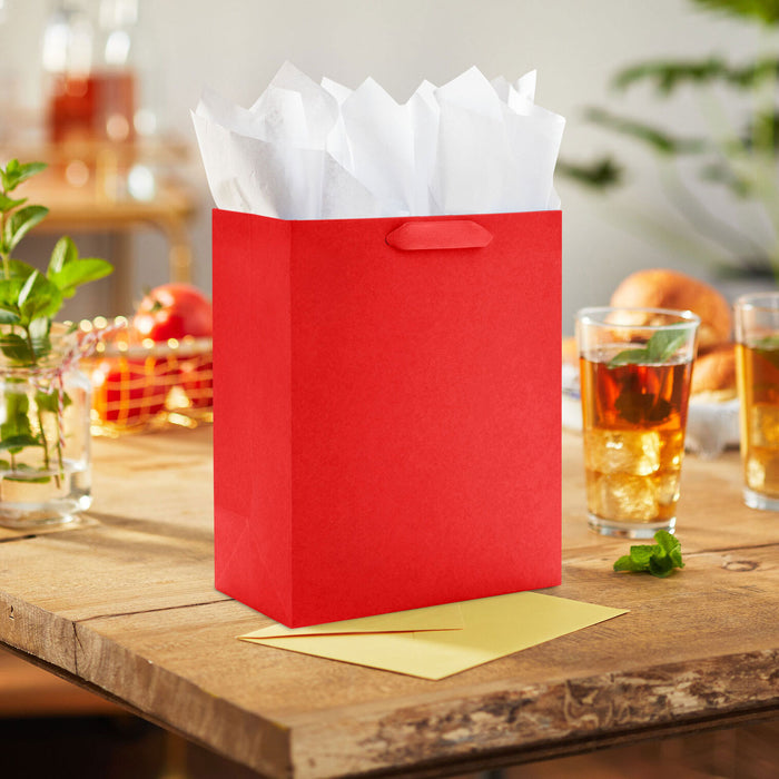 Red gift bag with white tissue paper on a wooden table with drinks and snacks.