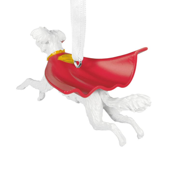 A white dog Christmas ornament wearing a red cape and yellow collar, hanging from a white ribbon on a plain white background.