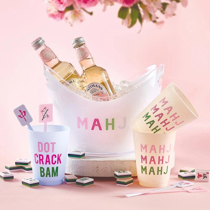 Beverage setup with bottles, cups, and 'MAHJ' glasses on a pink background