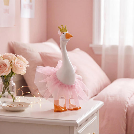 A white decorative goose figurine wearing a pink tutu and small gold crown, displayed on a white bedside table in a softly lit pink bedroom.