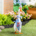 Decorative goose with a birthday hat and bib standing on grass with flowers and plants in the background