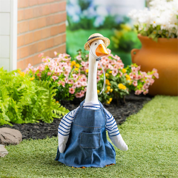 Decorative goose figurine wearing a blue apron and straw hat in a garden setting.