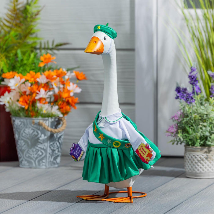 A decorative goose figurine dressed in a green and white outfit with a green beret, standing on a gray deck with potted plants in the background.