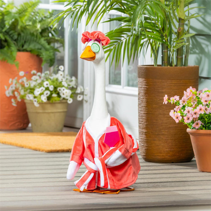 Toy goose in a red outfit on a wooden deck with potted plants in the background