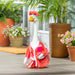 Toy goose in a red outfit on a wooden deck with potted plants in the background