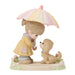 A pastel figurine of a young girl with a pink and cream umbrella, wearing a yellow raincoat and hugging a small tan dog on a decorative base.