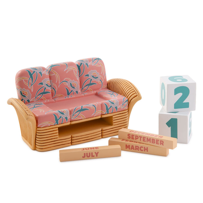 Toy wicker sofa with floral cushions and wooden age blocks on a white background