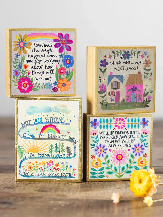 Four colorful greeting cards with floral designs and motivational text on a wooden surface.