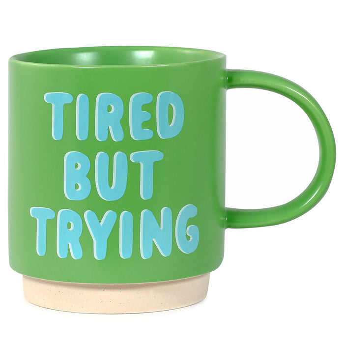 Green mug with 'TIRED BUT TRYING' text on a white background