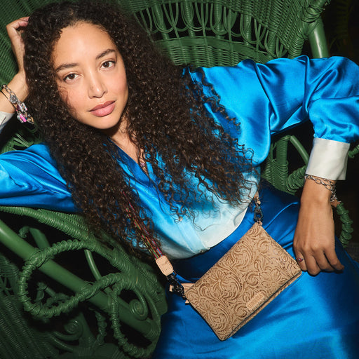 Woman in a blue dress sitting on a green chair holding a brown handbag.