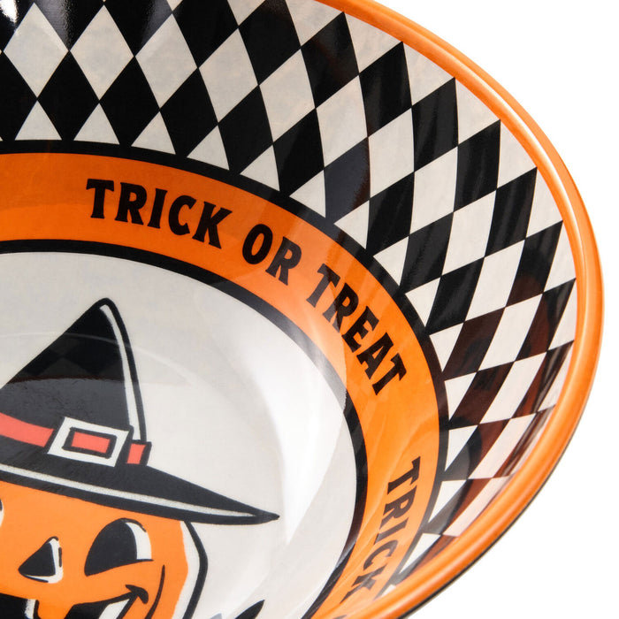 Close-up of a Halloween-themed bowl with a black and white checkered pattern, orange rim, and a jack-o'-lantern wearing a witch hat. The words 'TRICK OR TREAT' are printed around the orange band.