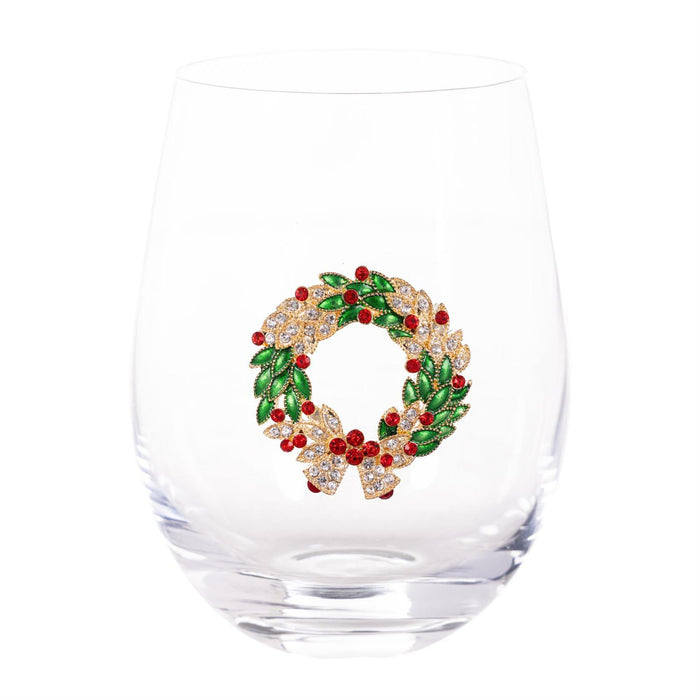 A clear stemless wine glass featuring a decorative holiday wreath design on the front, embellished with green leaves, red berries, and gold-toned rhinestone accents, set against a plain white background.