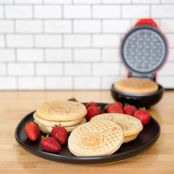 Waffle maker with waffles and strawberries on a plate against a tiled wall background