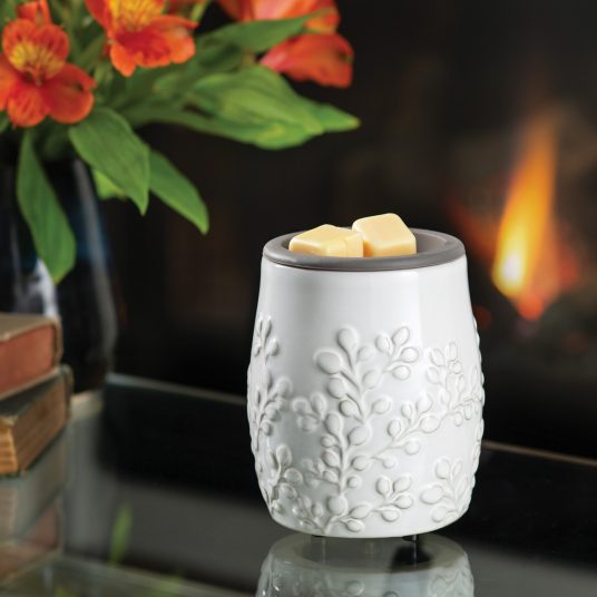 White textured wax warmer with flowers and a fireplace in the background