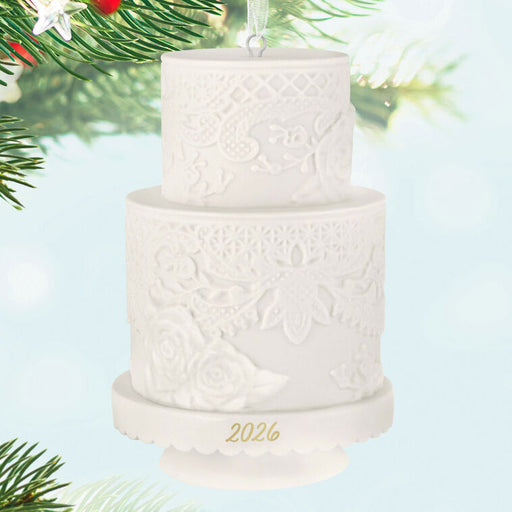 White two-tiered cake ornament with '2026' on a light blue background with Christmas tree branches.