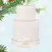White two-tiered cake ornament with '2026' on a light blue background with Christmas tree branches.
