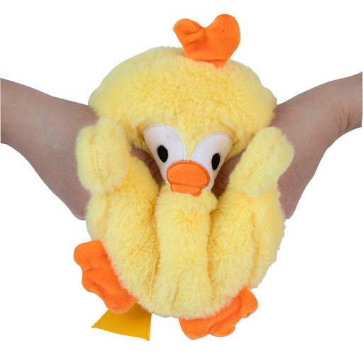 Plush duck toy with a yellow body and orange feet and beak, held between two hands on a white background.
