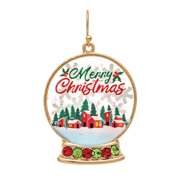 A gold-toned Christmas snow globe earring featuring a festive winter village scene with red cabins, evergreen trees, and 'Merry Christmas' lettering in green and red on a white background.