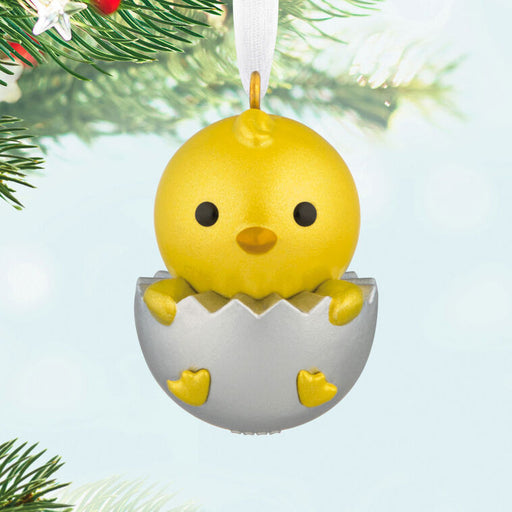 Yellow chick in an eggshell Christmas ornament on a tree branch.